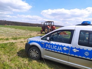 Radiowóz a w tle traktor podczas prac polowych