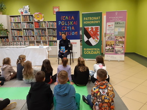 Policjantka czyta dzieciom książkę w Bibliotece Publicznej w Gołdapi